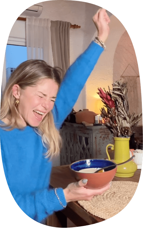 Pełna energii kobieta w niebieskim swetrze trzymająca miskę, siedzaca przy drewnianym stole.